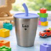 Personalized kids cup engraved with Leo, blue lid, surrounded by colorful toys