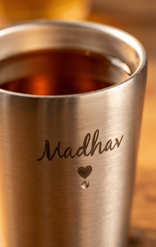 Close-up of engraved name Madhav on stainless steel cup showing detailed etching