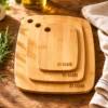 Personalised engraved bamboo chopping board on a worn oak kitchen countertop with fresh rosemary and cream linen tea towel in warm morning sunlight.
