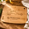 Personalised bamboo chopping board engraved with family name and special date on a rustic oak kitchen countertop with rosemary and linen cloth.