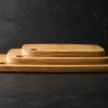 Three long grain bamboo chopping boards stacked in graduated sizes on a dark slate surface with visible layered thickness and dramatic side lighting.