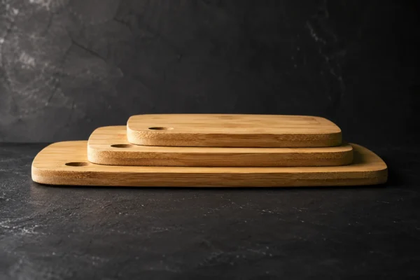 Three long grain bamboo chopping boards stacked in graduated sizes on a dark slate surface with visible layered thickness and dramatic side lighting.